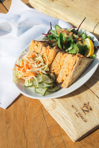 Crab sandwich with coleslaw and pickles on a white plate, placed on a wooden surface.